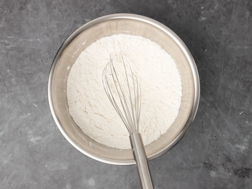 large round metal mixing bowl with white flour and a large metal wire whisk